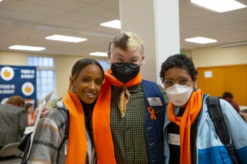 3 Hunger Action Day advocates pose with orange scarves