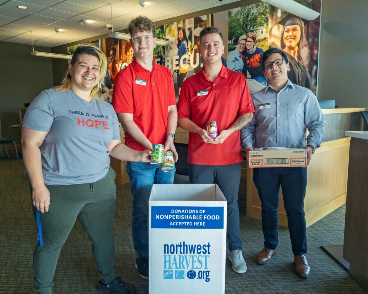 Northwest Harvest staff and BECU employees pose holding cans of food above a donation box