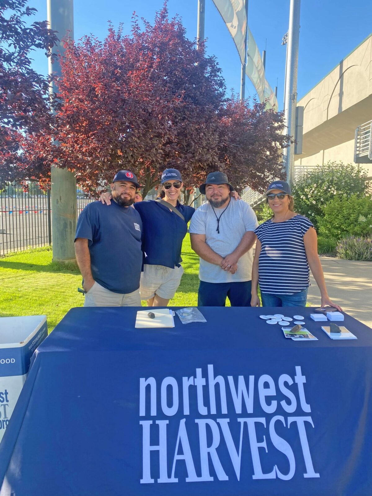 Northwest Harvest staff poses behind table outside at Pippins event