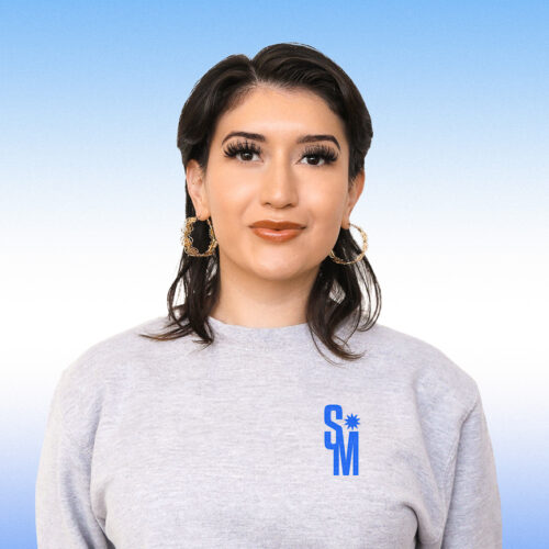 Santa Mercita subtly smiling in a grey long sleeve and large gold hoop earrings.