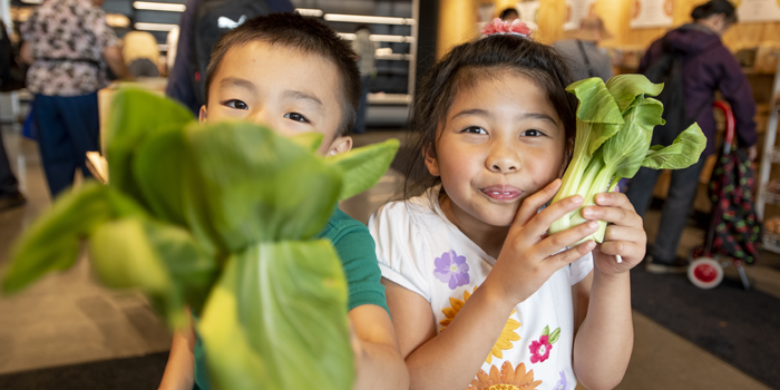 Two kids holding vegetables in SODO market