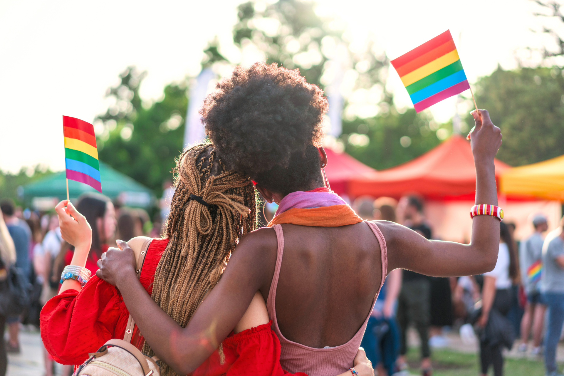 Rear view image of multi-ethnic couple embracing and waving rainbow flag at pride event