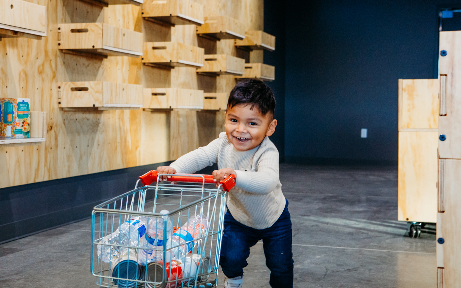 smiling child pushing mini grocery cart through market